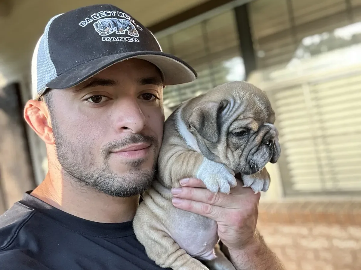 Jason Soares holding a fawn English bulldog puppy on his shoulder